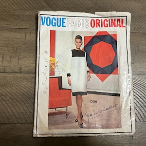 May include: Vintage Vogue Paris Original sewing pattern featuring a black, white, and gray color block dress design by Yves Saint Laurent. The pattern envelope includes the number 1556 and the Vogue Paris Original logo.