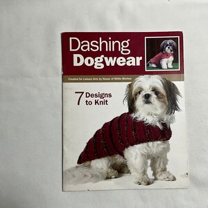 May include: Book cover with the title "Dashing Dogwear" and a small dog wearing a red knitted sweater. The book cover also includes the text "7 Designs to Knit" and "Created for Leisure Arts by House of White Birches".