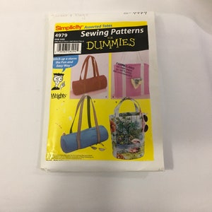 以下が含まれることがあります： Simplicityのトートバッグ用ソーイングパターンで、「Sewing Patterns for Dummies」と表示されています。茶色のダッフルバッグ、ピンクのトートバッグ、青色のダッフルバッグなど、さまざまなトートバッグのデザインのイラストが特徴です。パターンには「4979」と「ONE SIZE」と記載されています。