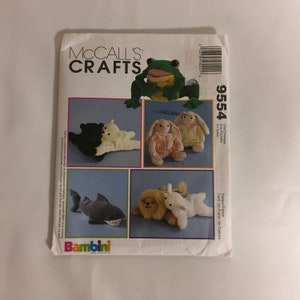 May include: A McCall's Crafts sewing pattern for stuffed animal toys. The pattern features a frog, bears, bunnies, a shark, and a lion with a lamb. The pattern is labeled "Bambini" and includes the number 9554.