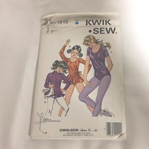 May include: A Kwik Sew pattern envelope 1213 for sizes 4, 5, 6, 7. The white paper envelope features illustrations of three figures wearing leotards and leggings in purple and orange tones, with text including Kwik Sew Pattern Co. Inc.
