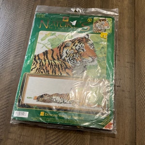 May include: A cross-stitch kit with two tiger designs. The kit shows a detailed image of a tiger's face and a second image of a tiger lying down. The packaging is green with the words "Nature's Window" and "Designs for the Needle".