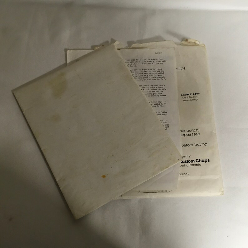 Op de afbeelding: Een witte envelop met een bruine vlek. De envelop is dubbelgevouwen en bevat een wit vel papier. Het papier bevat tekst die zegt "4 maten in elke Klein Medium Groot & Groot" en "pons. ippers (zie voordat u koopt am by custom Chaps erta, Canada uced)"