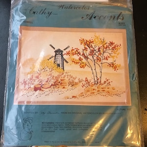 May include: A vintage embroidery kit featuring a watercolor design of a windmill and trees in autumn colors. The kit includes hand-silk screened halftone design on linen and cotton fabric, 100% Crewel wool yarns and embroidery floss, two needles, mounting board.  The kit is 5 inches by 7 inches and is unassembled.  The kit is labeled "Cathy Inc. Watercolor Accents K003".