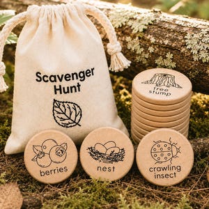 May include: A cream-colored canvas drawstring bag with the text Scavenger Hunt and a leaf illustration, accompanied by a stack of round wooden tokens and three individual tokens featuring black line drawings of berries, a nest, and a crawling insect.
