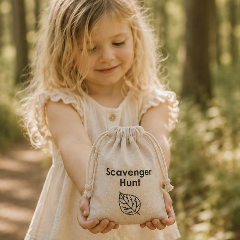 May include: A small, off-white canvas drawstring pouch featuring the black printed text Scavenger Hunt and a simple line drawing of a leaf centered on the front. The bag is made of a woven fabric and has two thick, matching cotton drawstrings.