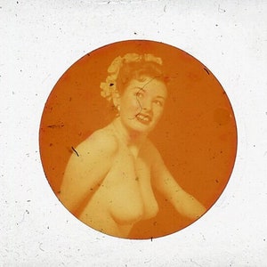 May include: Vintage sepia-toned photograph of a woman in a circular frame. The woman is smiling, with flowers in her hair. The image has a retro aesthetic, with visible scratches and imperfections.