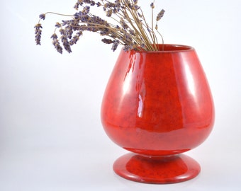 May include: A red ceramic vase with a wide base and a rounded body, holding a bouquet of dried lavender.