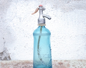 Pode incluir: Uma garrafa de vidro azul vintage com um sifão de metal e uma tampa de plástico vermelha. A garrafa tem o texto "Siphon Hercules" impresso nela.