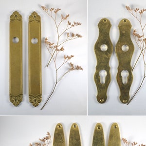 May include: Four antique brass door plate escutcheons with keyhole cutouts. Two are rectangular with ornate edges and two are oval.