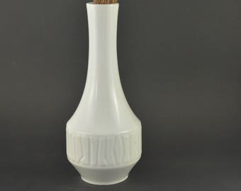 May include: A white ceramic vase with a textured design, holding a bouquet of dried lavender.
