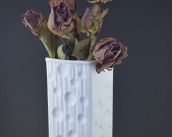May include: A white ceramic vase with a textured surface and a bouquet of dried roses.