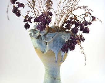May include: A ceramic vase with a unique, organic shape and a light blue and yellow glaze. The vase is filled with dried flowers and grasses.