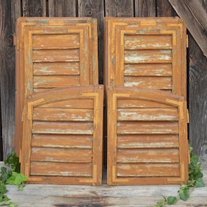 Puede incluir: Cuatro contraventanas de madera con un acabado marrón desgastado. Las contraventanas tienen un diseño de listones y están dispuestas en dos pares, siendo el par superior ligeramente más grande que el par inferior.