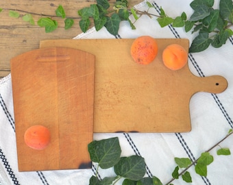 May include: Two wooden cutting boards, one with a handle, on a white and black striped tablecloth with green ivy leaves and three orange apricots.