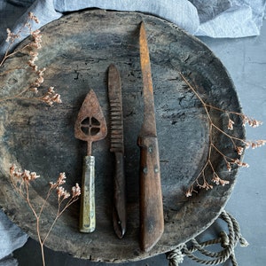 Puede incluir: Tres herramientas de cocina vintage sobre una superficie de madera rústica. Una espátula de metal oxidada, un cuchillo de metal oxidado y un raspador de metal oxidado con mango de madera.