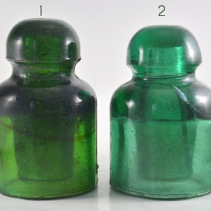 Puede incluir: Dos tapones de botella de vidrio verde, uno con un tono de verde ligeramente más oscuro que el otro.