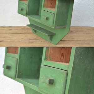 May include: A green wooden wall shelf with two drawers and a small shelf. The shelf has a rustic, vintage look.