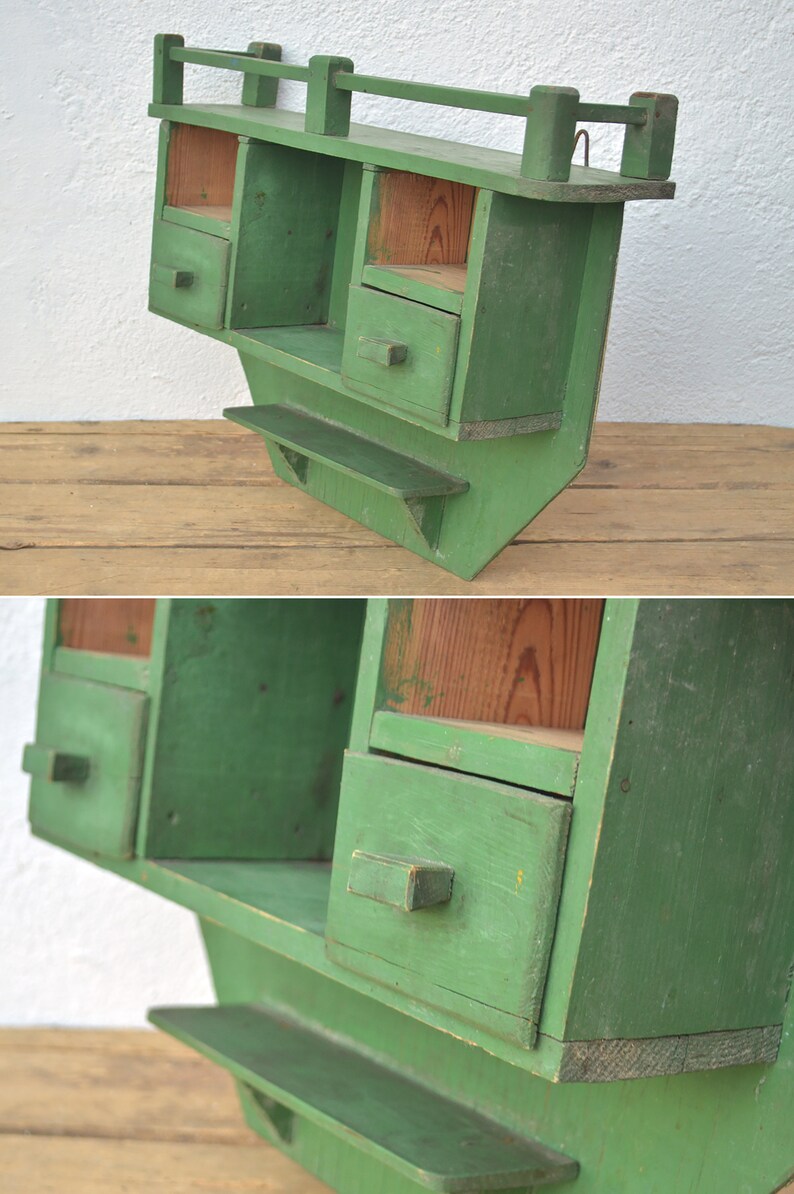 May include: A green wooden wall shelf with two drawers and a small shelf. The shelf has a rustic, vintage look.