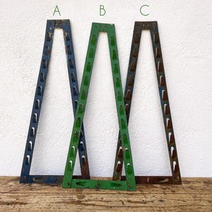 Puede incluir: Tres marcos metálicos en forma de triángulo. Los marcos están pintados en diferentes colores: azul, verde y marrón oxidado. Los marcos están dispuestos en fila, con el marco azul a la izquierda, el marco verde en el centro y el marco marrón oxidado a la derecha.