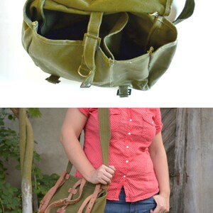 May include: A green canvas messenger bag with brown leather straps and buckles. The bag has a flap closure and a zippered pocket on the front.