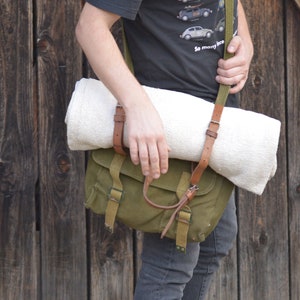 May include: A person wearing a black t-shirt with a print of various Volkswagen Beetles and the text "So many ice". They are carrying a green canvas bag with a brown leather strap and a white towel.