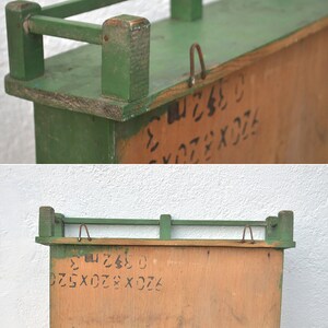 May include: A green wooden shelf with a metal railing. The shelf has a wooden back with handwritten numbers and letters. The shelf is 17.75 inches wide and 9.75 inches tall.