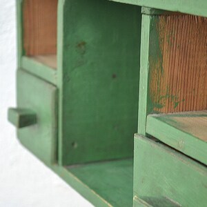 May include: A green wooden shelf unit with two drawers and open shelves. The shelves are made of wood and have a rustic look.