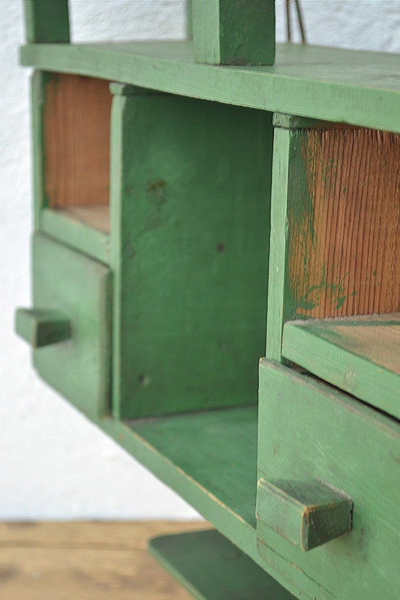 May include: A green wooden shelf unit with two drawers and open shelves. The shelves are made of wood and have a rustic look.