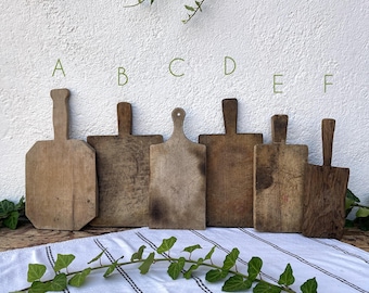 May include: Six wooden cutting boards of various shapes and sizes, arranged in a row on a white and black striped tablecloth. The boards are all made of natural wood and have a rustic, vintage look.