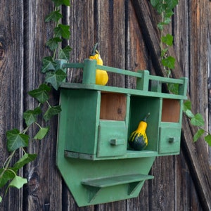 May include: A green wooden shelf with three compartments and a lower shelf. The shelf is attached to a wooden wall and has two gourds on it, one yellow and one green.