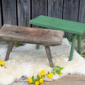 May include: Two wooden stools, one painted green and one natural wood, sit on a white sheepskin rug with yellow flowers.