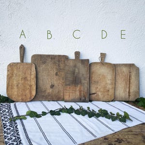 Pode incluir: Cinco tábuas de corte retangulares de madeira rotuladas como A, B, C, D e E. As tábuas variam em tamanho e forma, apresentando texturas desgastadas, veios de madeira visíveis e tons castanhos naturais. Algumas incluem pegas ou orifícios.