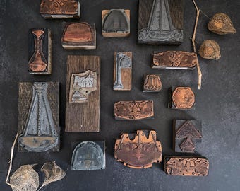 May include: A collection of vintage woodblock printing stamps with various designs, including floral, geometric, and abstract patterns. The stamps are made of wood and metal and have a rustic, antique look.