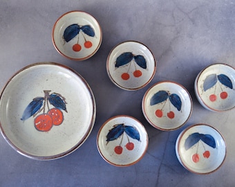 Pode incluir: Conjunto de sete tigelas de cerâmica com um esmalte salpicado e um desenho de cerejas. As tigelas são de vários tamanhos, sendo a maior com um único ramo de cerejeira e as menores com duas cerejas.
