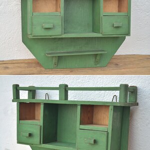 May include: A green wooden wall shelf with three compartments and a lower shelf. The shelf has a decorative railing on the top.