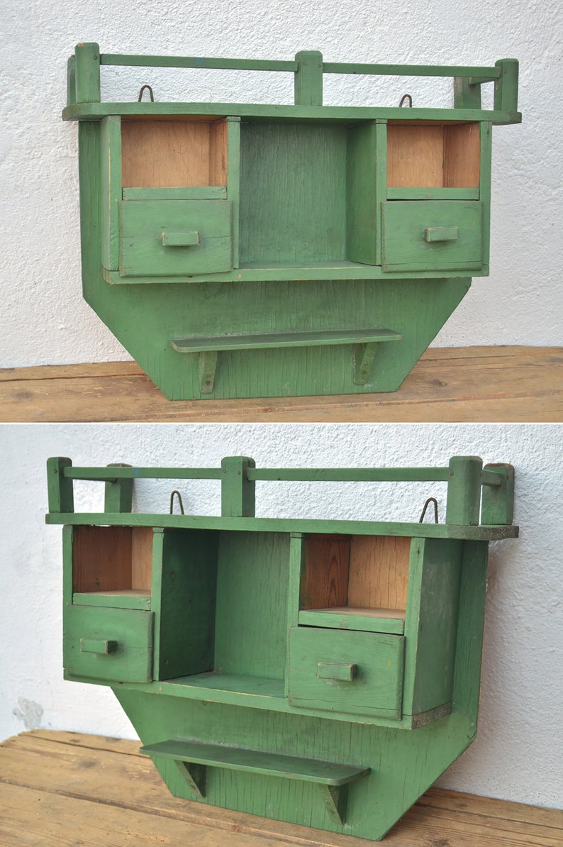 May include: A green wooden wall shelf with three compartments and a lower shelf. The shelf has a decorative railing on the top.