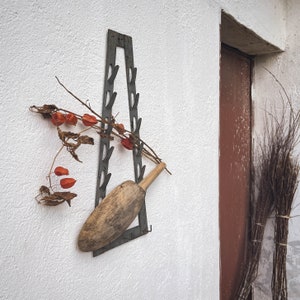 Puede incluir: Un estante de metal con ganchos fijado a una pared blanca. Un rodillo de madera cuelga del estante. Flores secas y linternas de papel rojas cuelgan del estante.