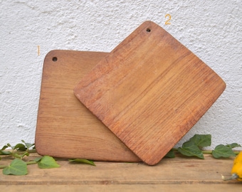 May include: Two wooden cutting boards, one on top of the other, both with a square shape and a hole in the top. The boards are made of light brown wood and have a rustic appearance.