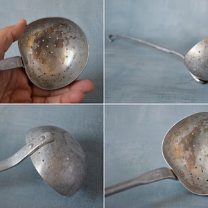 Puede incluir: Un cucharón vintage de aluminio con un mango largo y un tazón perforado. El cucharón tiene un aspecto desgastado y envejecido y es perfecto para servir sopa u otros líquidos.