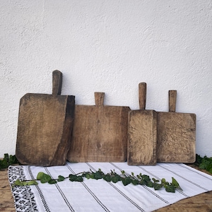 May include: Four rectangular wooden chopping boards with handles, each featuring a distinct brown wood grain and weathered texture. The boards vary in size and shape, displaying natural wear and surface markings from use, arranged in a row.