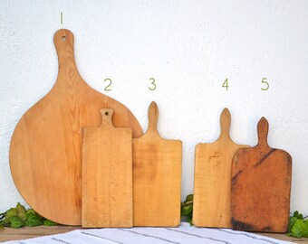 May include: Five wooden cutting boards of varying sizes and shapes. The largest board is round with a long handle. The other boards are rectangular with handles. The boards are all made of light wood and have a natural finish.