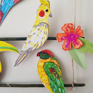 May include: Hand-drawn paper cutouts of colorful birds and a flower. The birds include a yellow cockatiel with a red cheek patch, and a green, yellow, and red parrot. The flower is orange and pink with green leaves.