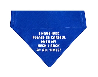 May include: A triangular royal blue pet bandana featuring white text that reads: I HAVE IVDD PLEASE BE CAREFUL WITH MY NECK & BACK AT ALL TIMES! The fabric has visible stitched edges along the top border and a pointed bottom hem.