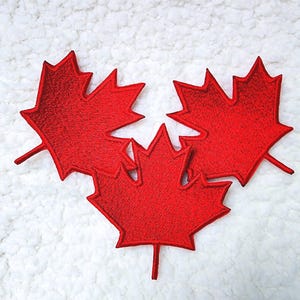 Peut inclure: Trois écussons de feuilles d'érable rouges brodées, avec des tiges, sur un fond blanc texturé. Les feuilles sont d'un rouge vif et présentent des coutures détaillées.