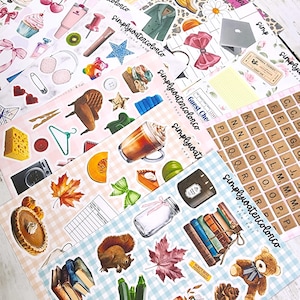 May include: A collection of decorative stickers with various illustrations, including food, books, and seasonal items. The stickers feature a variety of colors and designs, with some including text. The stickers are arranged on a light-colored surface.