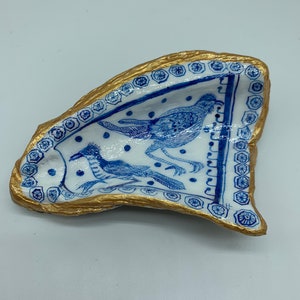 Puede incluir: Un plato de cerámica blanca con un diseño azul y dorado. El plato tiene forma de pájaro y un borde dorado. El diseño presenta dos pájaros con cuellos y patas largos.