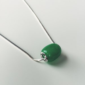 May include: A silver chain necklace featuring a vibrant green, oval-shaped bead pendant. The bead has a glossy finish and is attached to the chain with silver-toned metal findings. The necklace is displayed against a white background.