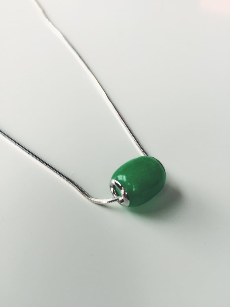 May include: A silver chain necklace featuring a vibrant green, oval-shaped bead pendant. The bead has a glossy finish and is attached to the chain with silver-toned metal findings. The necklace is displayed against a white background.