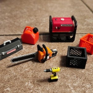 Könnte beinhalten: Eine Sammlung von Miniaturwerkzeugen, darunter eine Kettensäge, eine Werkzeugkiste, ein Kanister, eine Bohrmaschine, ein Generator mit der Aufschrift "HONDA" und zwei Drahtgitterkästen, einer orange und einer schwarz.